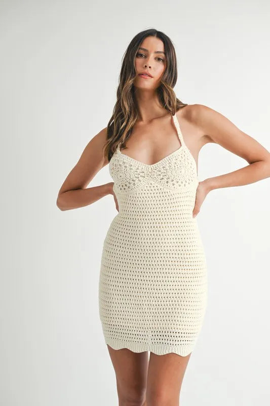Model in fitted beige crochet mini dress featuring crisscross tie-back straps and body-hugging silhouette. Perfect for summer days or beach parties.